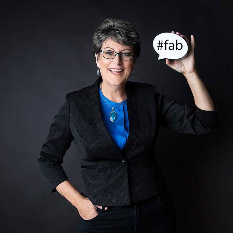 Ingrid Moyle in a dark suit and blue shirt holding a hashtag #fab.