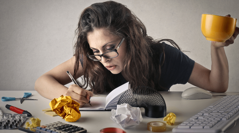 Woman intensely writing in a notebook surrounded by scrunched paper